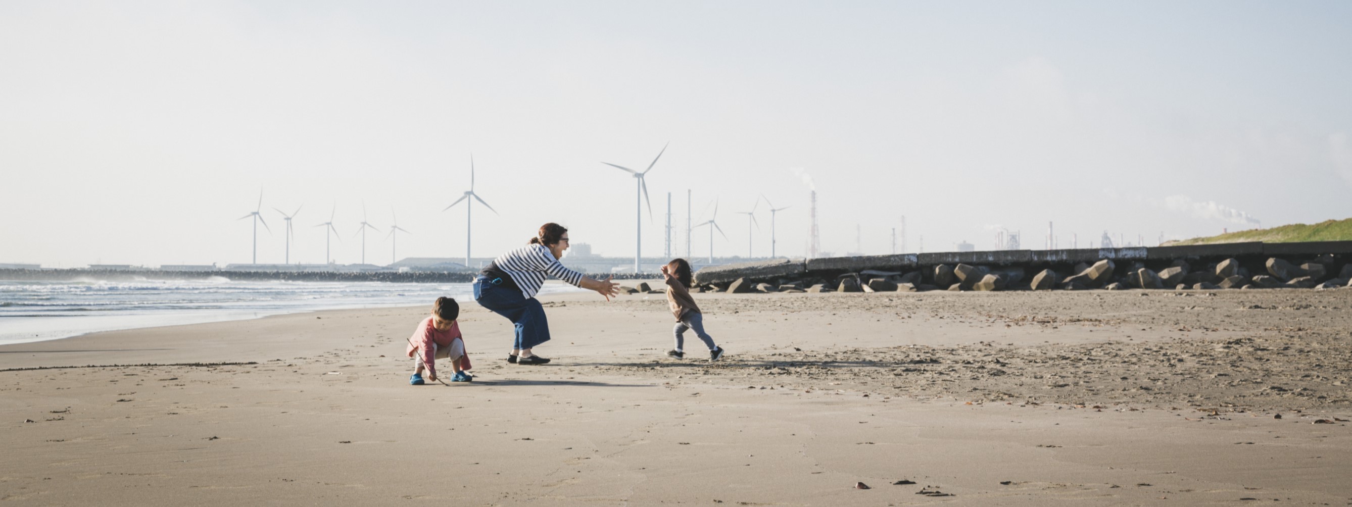 A family playing on a beach with wind turbines in the background