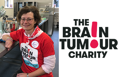 Sally is smiling sitting at a stainless steel kitchen unit in a red 'The Brain Tumour Charity' t-shirt.